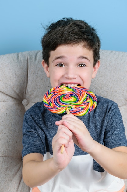 Enfant de 8 ans mordant et souriant une grosse sucette colorée et regardant la caméra.