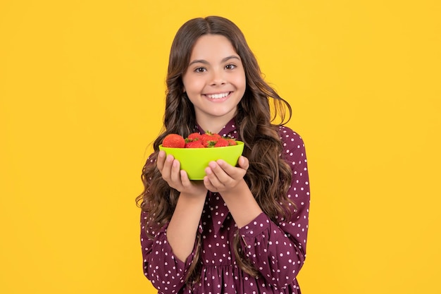 Un enfant adolescent heureux tient un bol de fraises sur fond jaune