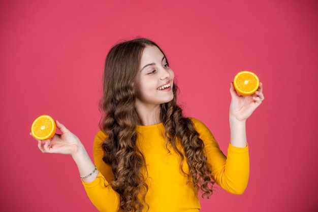 Un enfant adolescent heureux tient des fruits orange sur fond rose