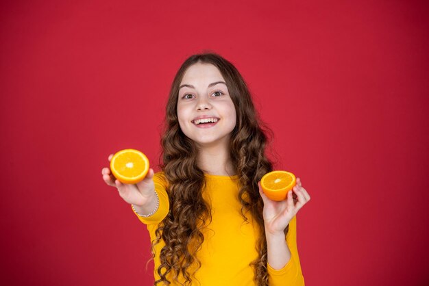 Un enfant adolescent joyeux tient des fruits orange sur fond violet