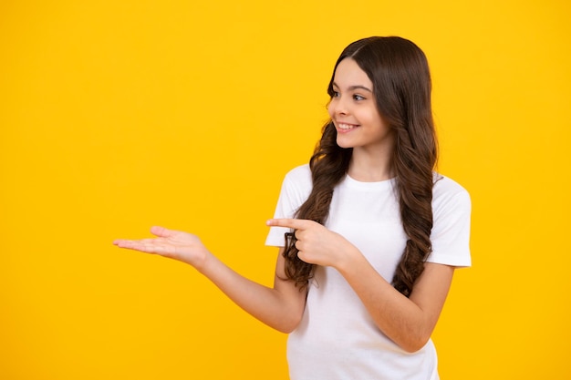 Enfant adolescent pointant vers le côté avec un doigt pour présenter un produit ou une idée Adolescente en tenue décontractée pointant vers l'espace vide Heureux adolescent émotions positives et souriantes d'une adolescente