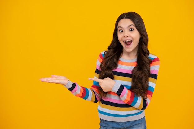 Enfant adolescent pointant vers le côté avec un doigt pour présenter un produit ou une idée Adolescente en tenue décontractée pointant vers l'espace vide