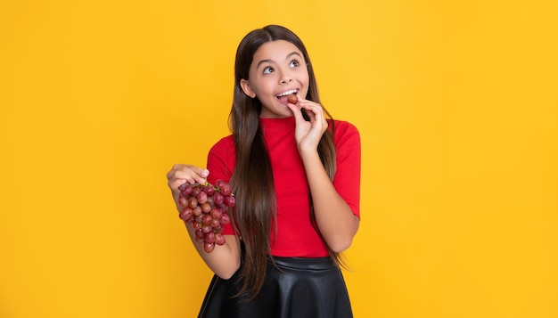 Un enfant adolescent souriant tient une grappe de raisin sur fond jaune