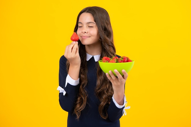 Un enfant adolescent tient un bol de fraises sur fond jaune