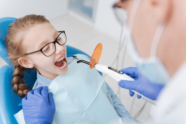 Enfant adorable assez enthousiaste tenant sa bouche ouverte lors de la visite de son dentiste et blanchissant ses dents