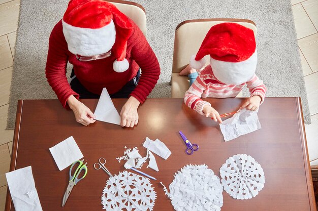 Un enfant et un adulte se préparent pour le nouvel an et Noël en découpant des flocons de neige décoratifs dans des serviettes. vue de dessus.