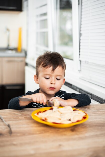 Enfant affamé mangeant des boulettes dans la cuisine, se reposant à la table dans une veste grise