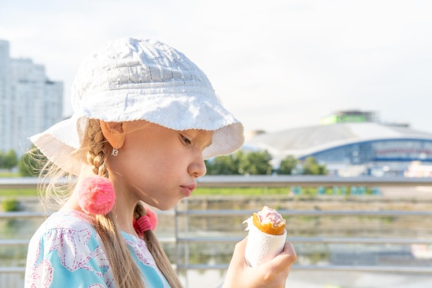 Enfant affamé mangeant de la nourriture de rue sur la plage en été Une fille dans un chapeau mangeant des saucisses frites