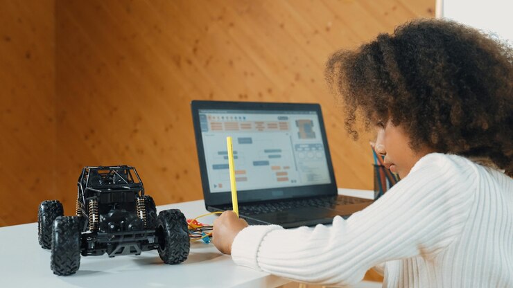 Photo un enfant africain écrit la structure d'un modèle de voiture tandis qu'un ordinateur portable affiche le code de l'érudition