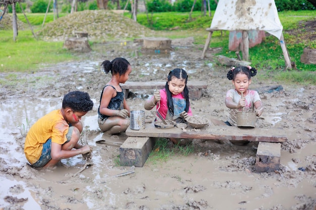 Enfant africain et fille asiatique jouant dans la boue de la flaque d'eau ensemble à l'apprentissage d'un camp d'été en plein air