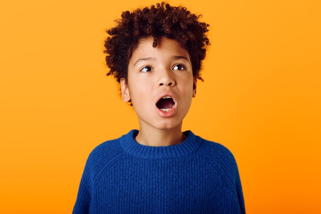 Un enfant afro-américain étonné avec une expression large et une bouche ouverte sur un fond orange vif.
