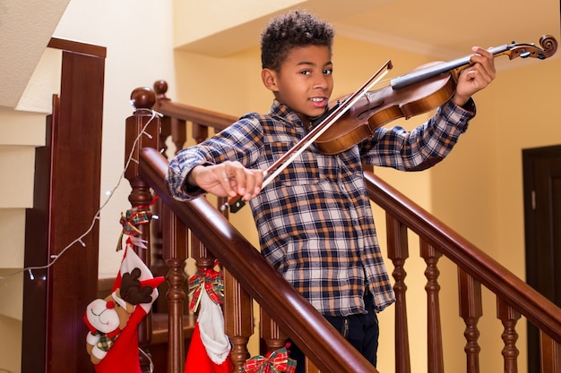 Un enfant afro souriant joue du violon Un garçon jouant du violon à Noël Les jeunes violonistes sourient le vrai Noël ...