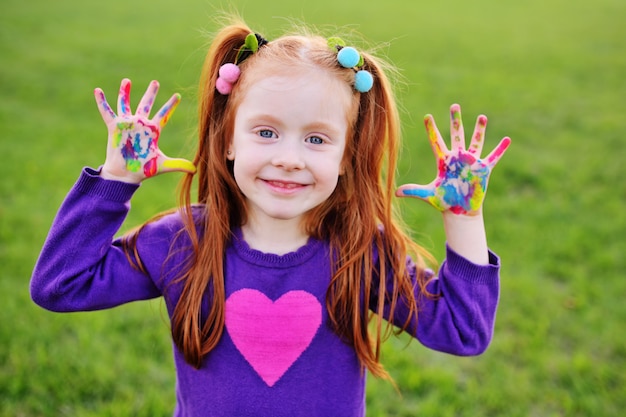 Enfant d&#39;âge préscolaire aux cheveux roux montrant des paumes souillées de peintures aux doigts multicolores