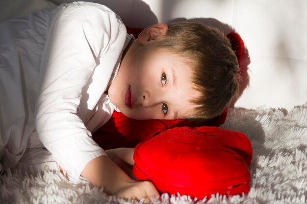 Enfant d'âge préscolaire fatigué Le garçon se trouve sur un oreiller rouge