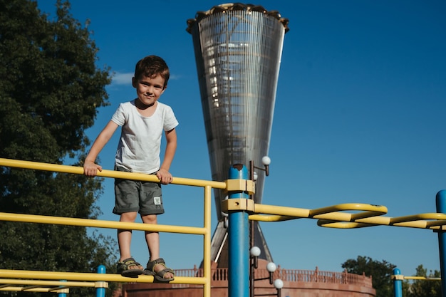 enfant d'âge préscolaire garçon joue sur des barres horizontales sur l'aire de jeux dans le parc en été