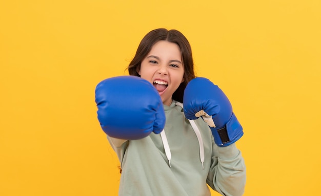 Enfant agressif frappant dans des gants de boxe sur fond jaune, sport