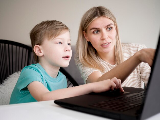 Photo enfant à l'aide de son ordinateur portable à l'intérieur à côté de sa mère