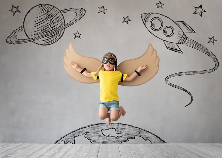 Photo enfant avec des ailes en papier sautant contre le mur de béton gris.