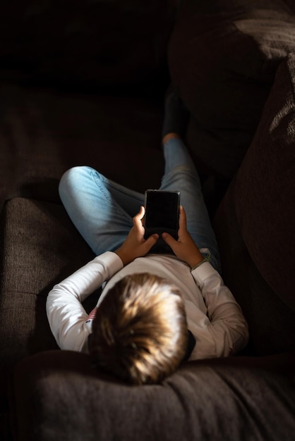 Photo un enfant allongé sur le canapé qui regarde un téléphone portable les parents s'inquiètent de l'obsession des enfants