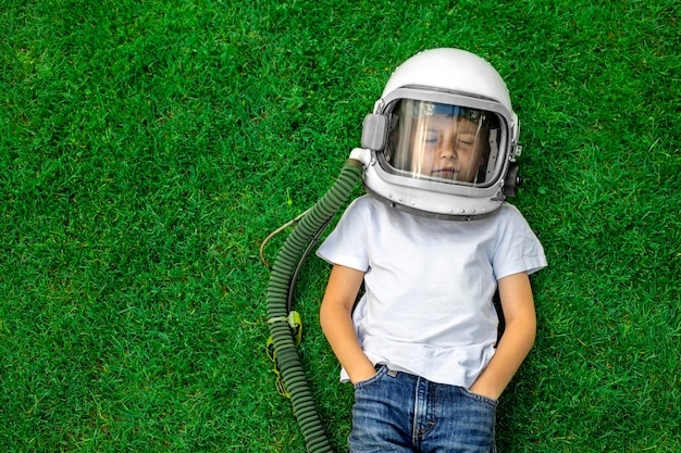 Un enfant allongé sur l'herbe, coiffé d'un casque d'astronaute, rêve de grandes réalisations !