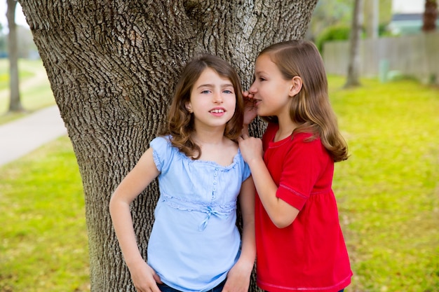 enfant ami filles chuchotant oreille jouant dans un arbre de parc