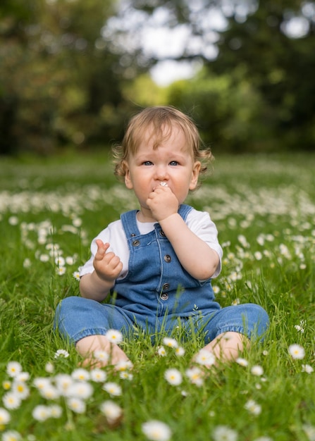 un enfant d'un an aux cheveux blonds ondulés est assis sur l'herbe verte parmi de nombreuses marguerites