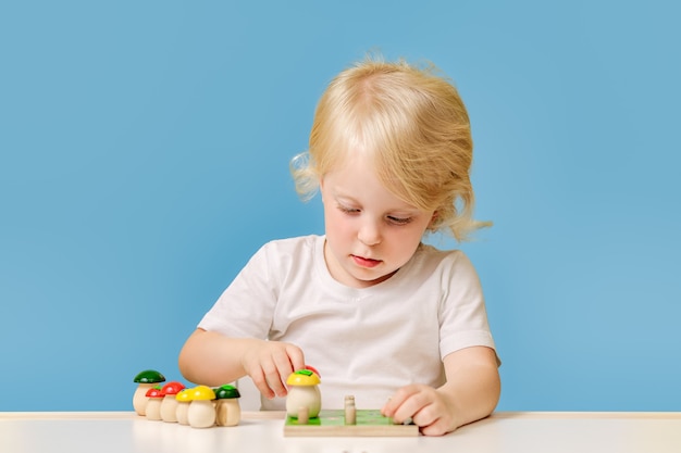 Un enfant d'un an joue à une table avec un jouet éducatif coloré sur fond bleu