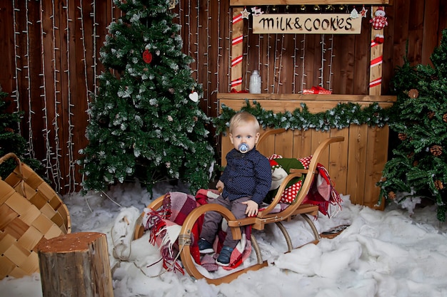 Un enfant d'un an joue sur un traîneau à l'arbre de Noël. Garçon mignon dans la salle décorée de Noël
