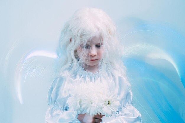 Enfant d'ange. L'innocence de l'enfant. L'énergie spirituelle. Pur rêve. Jolie petite fille blonde paisible avec des fleurs blanches dans une lueur de néon bleu sur fond d'espace vide clair.