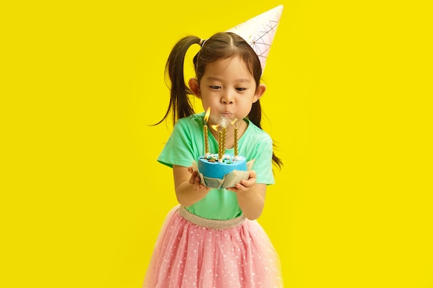 Un enfant d'apparence chinoise de cinq ans dans un chapeau de fête souffle des bougies sur un gâteau d'anniversaire