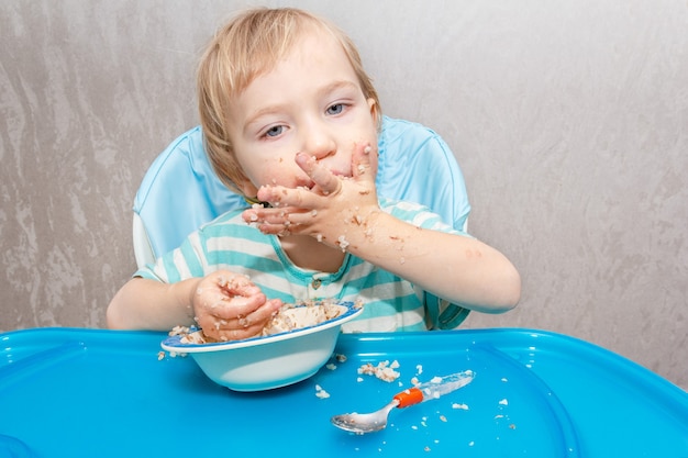 L'enfant apprend à manger indépendamment, l'enfant mange de la bouillie de sarrasin avec ses mains