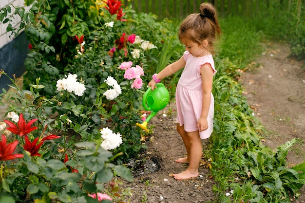 L'enfant arrose des fleurs dans un parterre de fleurs à partir d'un arrosoir vert en plastique jouet