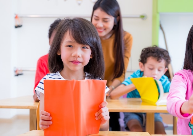 Enfant asiatique fille lecture livre dans la salle de classe et tandis que le professeur enseigner aux amis à côté d&#39;eux