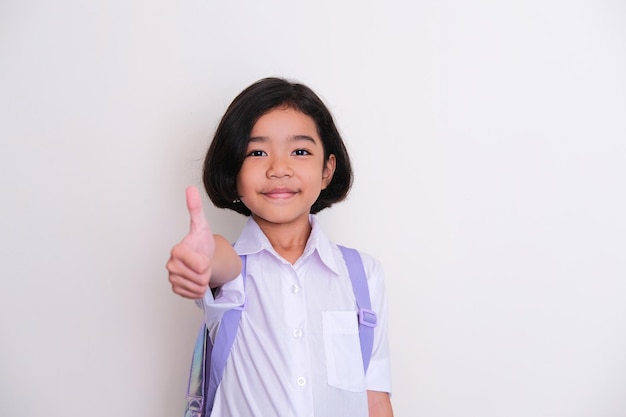 Photo enfant asiatique portant l'uniforme scolaire et sac à dos souriant et donnant le pouce vers le haut