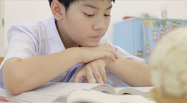 Enfant asiatique en uniforme d&#39;étudiant à faire ses devoirs à la maison.