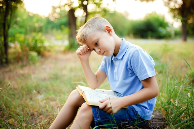 Enfant assis dans la forêt avec un livre sur les genoux.