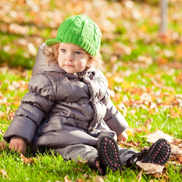 Enfant assis sur l'herbe dans le parc en automne