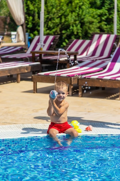 L'enfant assis près de la piscine se joue avec un pistolet à eau. mise au point sélective