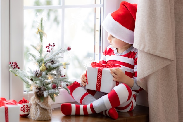 Enfant assis sur le rebord de la fenêtre Heureux enfant portant un pyjama de Noël