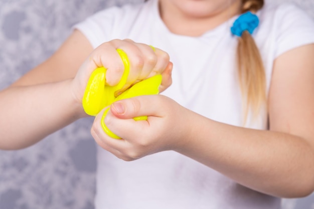 L'enfant aux cheveux blonds joue avec du mucus. Petite belle fille caucasienne joue avec du slime jaune. Jouer au jouet slime