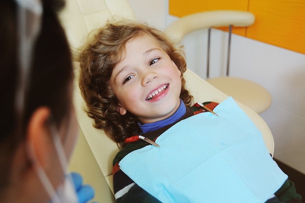 Un Enfant Aux Cheveux Bouclés Se Laisse Aller Et Grimace Dans Un Fauteuil Dentaire