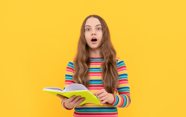 Un enfant aux yeux ouverts surpris tient un livre d'école surprise sur fond jaune