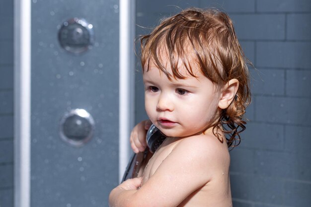 Enfant en bas âge dans une baignoire baignant l'enfant heureux de bébé avec de la mousse de savon sur la tête