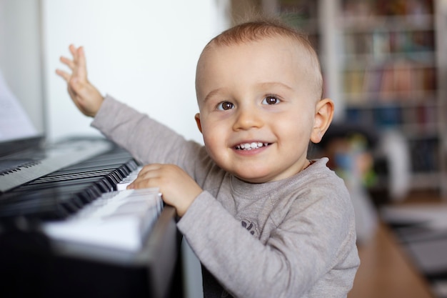 Un enfant en bas âge est debout au piano et souriant.