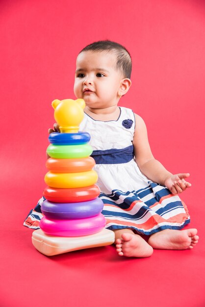 Enfant en bas âge indien ou asiatique ou nourrisson ou bébé jouant avec des jouets ou des blocs en position couchée ou assise isolé sur fond clair ou coloré