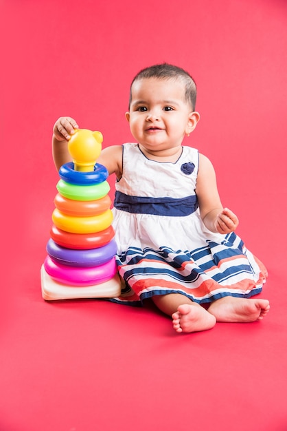 Enfant en bas âge indien ou asiatique ou nourrisson ou bébé jouant avec des jouets ou des blocs en position couchée ou assise isolé sur fond clair ou coloré
