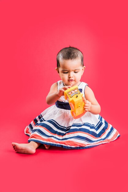 Enfant en bas âge indien ou asiatique ou nourrisson ou bébé jouant avec des jouets ou des blocs en position couchée ou assise isolé sur fond clair ou coloré