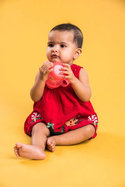 Enfant en bas âge indien ou asiatique ou nourrisson ou bébé jouant avec des jouets ou des blocs en position couchée ou assise isolé sur fond clair ou coloré