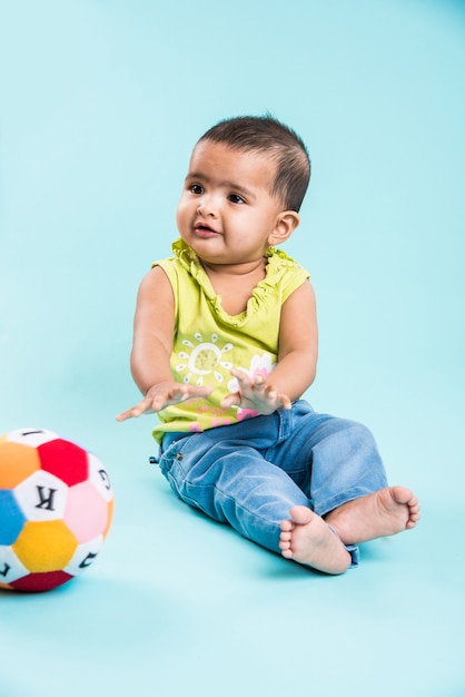 Enfant en bas âge indien ou asiatique ou nourrisson ou bébé jouant avec des jouets ou des blocs en position couchée ou assise isolé sur fond clair ou coloré