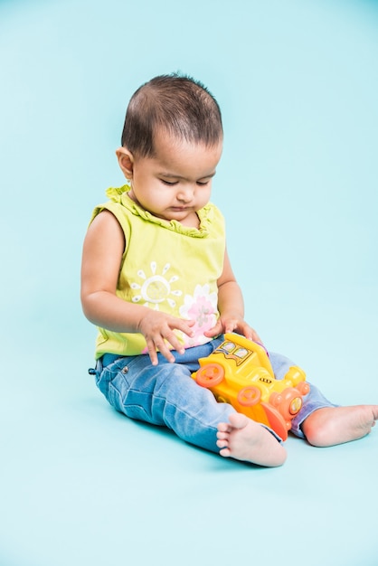 Enfant en bas âge indien ou asiatique ou nourrisson ou bébé jouant avec des jouets ou des blocs en position couchée ou assise isolé sur fond clair ou coloré